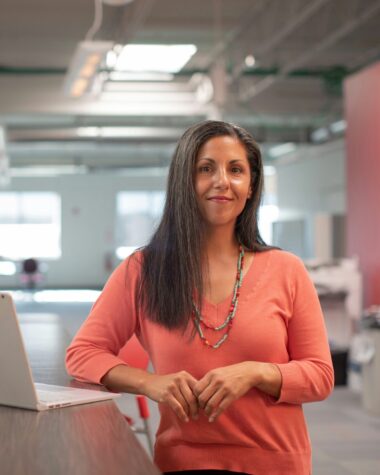 Mulher posando para a câmera apoiada em uma mesa de escritório